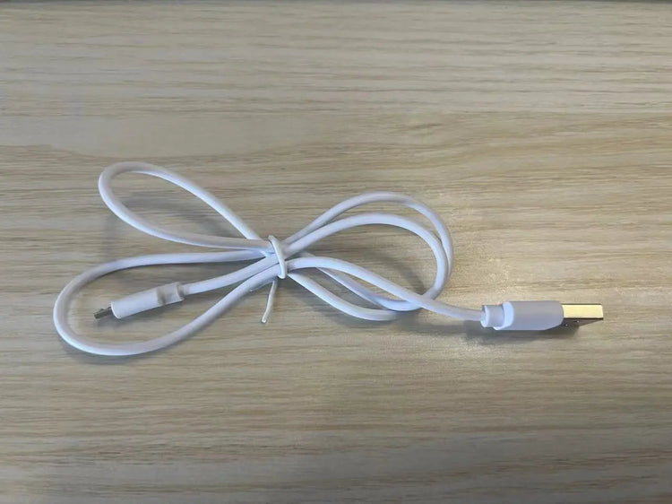 Charging cable for LED Face & Neck Lifting Massager on wooden surface.